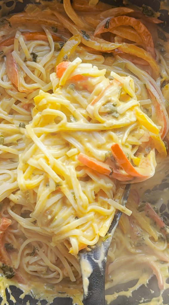 sliced bell peppers with cilantro, basil, and green onions added with garlic minced with coconut milk, Thai red curry paste, tomato paste, soy sauce all stirred together and rice noodles being completely coated in the curry